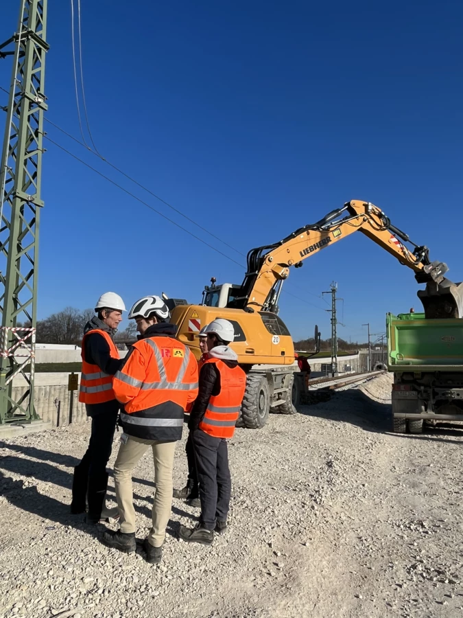 Bauarbeiter in Warnwesten vor Liebherr-Bagger beim Beladen eines Lkw (Rankweil, Deutschland)