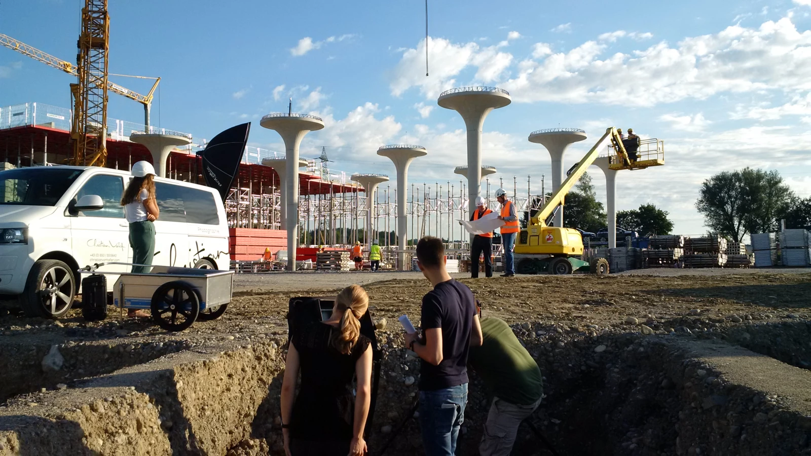 Arbeiter auf einer Baustelle mit vielen Betonsäulen und Kränen, während ein Fotoshooting stattfindet.