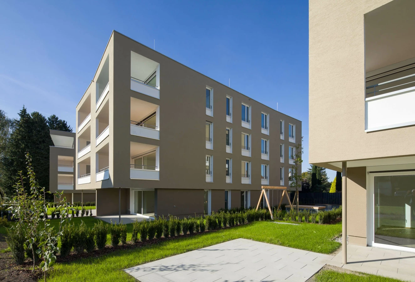 Moderne Wohnanlage Widum in Lustenau mit beigefarbener Fassade, Balkonen, Fenstern und gepflegter Grünfläche
