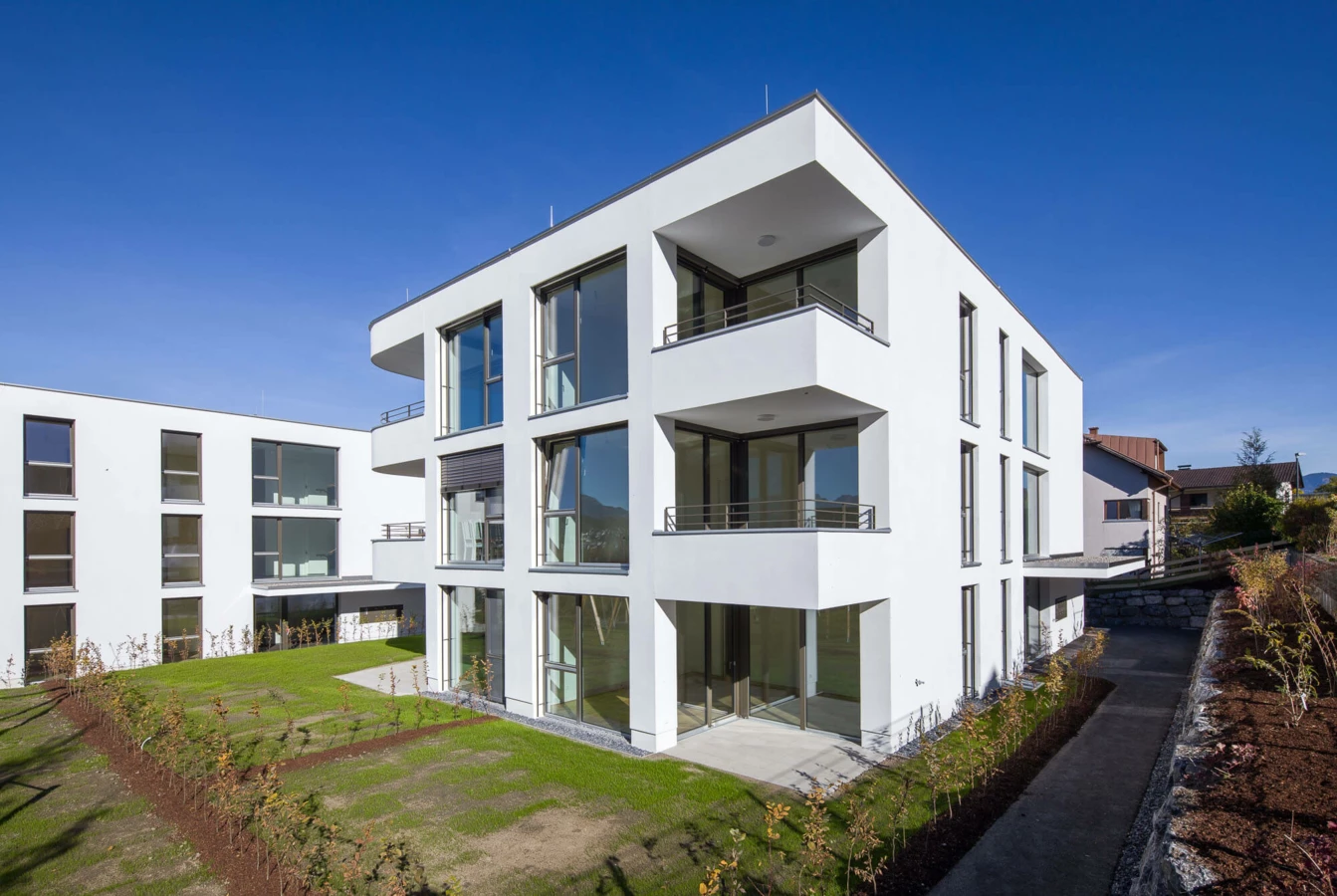 Moderne weiße Wohnanlage mit Balkonen und großen Fenstern unter blauem Himmel in Feldkirch (Wolf-Huber-Straße).