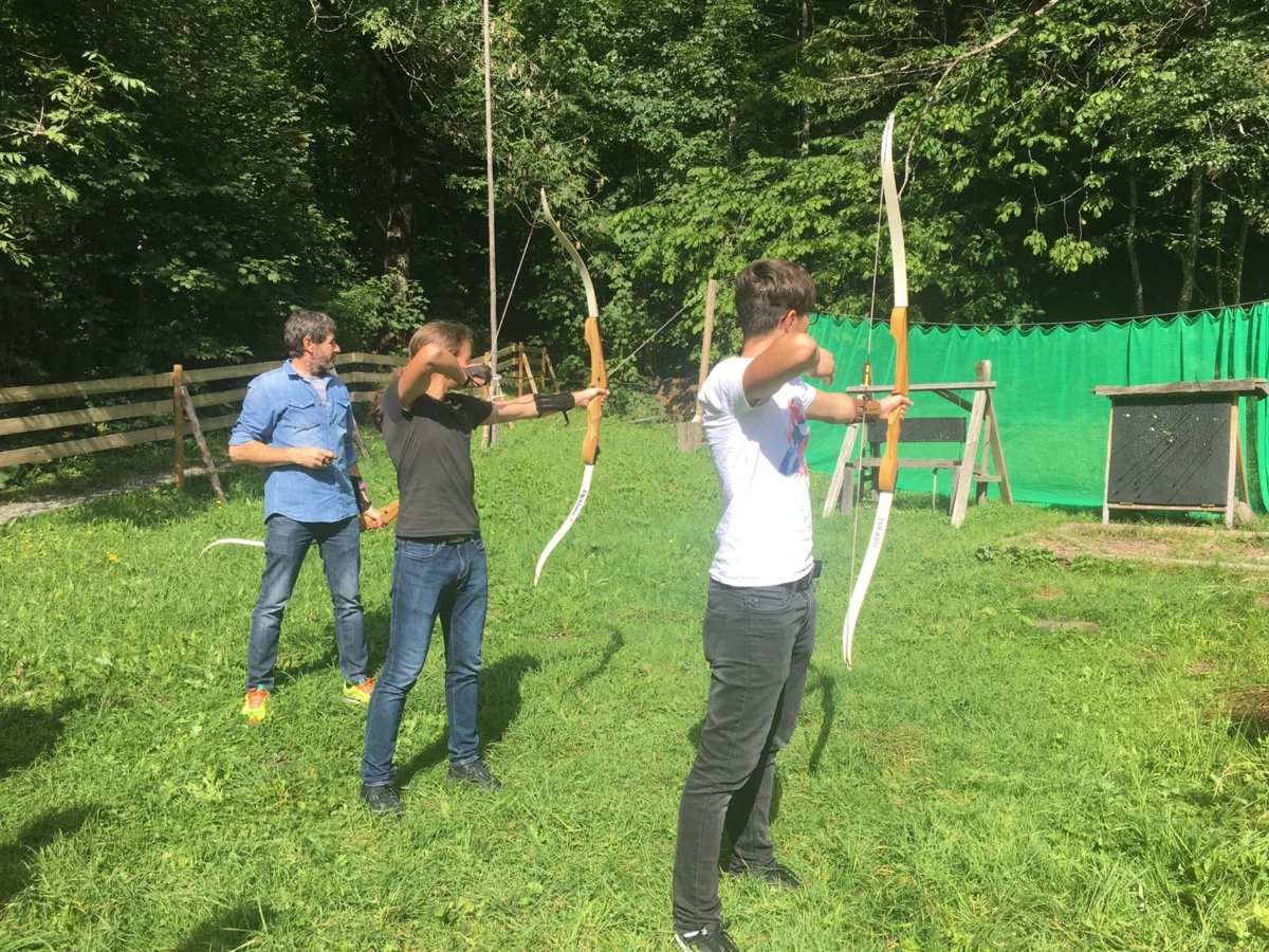 Drei Personen, vermutlich Lehrlinge, beim Bogenschiessen im Freien, konzentriert auf das Ziel.