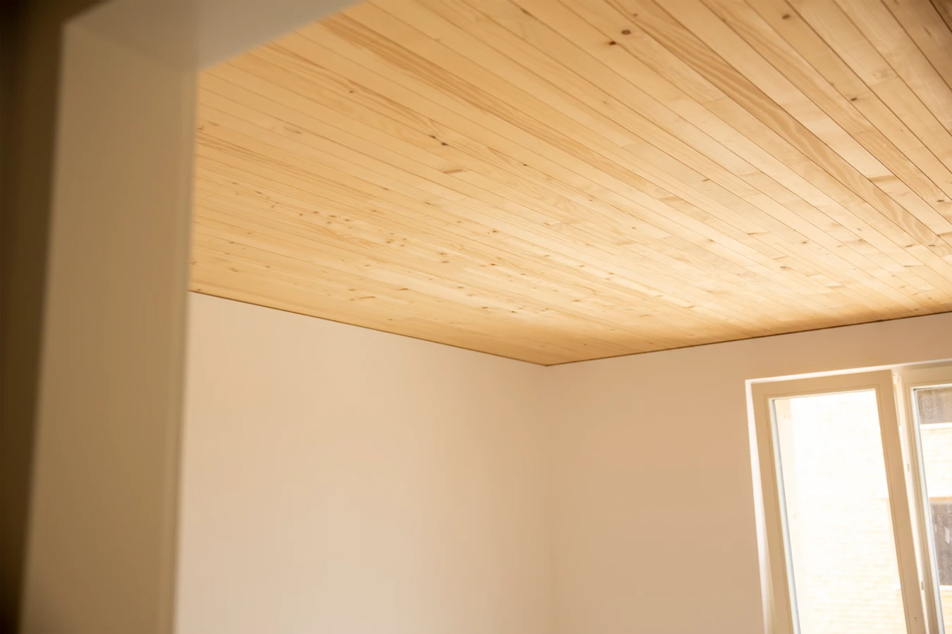 Eine helle Wand und eine Fensterfront in einem Zimmer mit einer Holzdecke an der Hellbrunnerstraße (Hellbrunnenstraße).