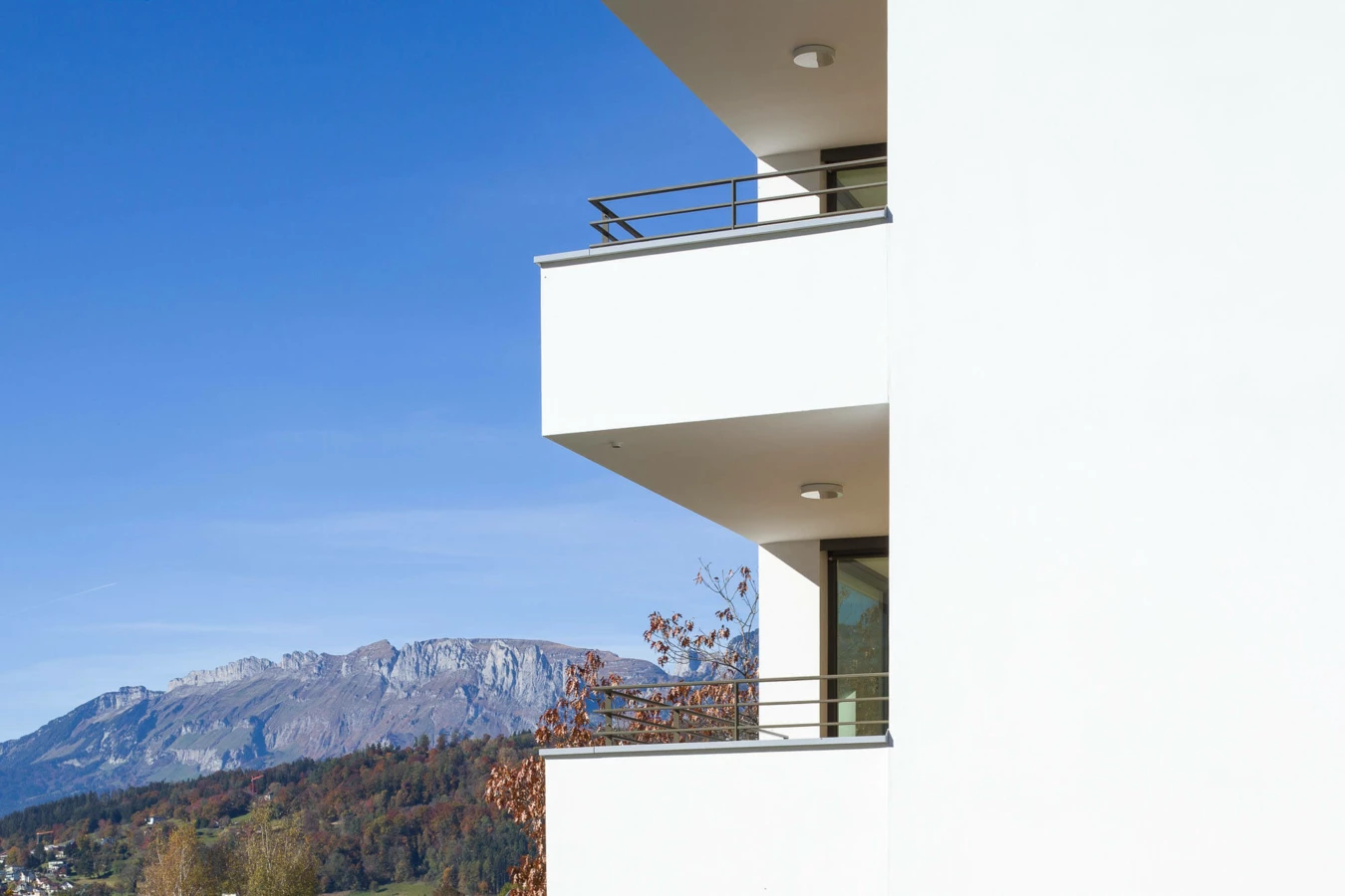 Moderne weiße Balkone eines Mehrfamilienhauses mit Bergblick an der Wolf-Huber-Straße in Feldkirch unter blauem Himmel (Wohnanlage).