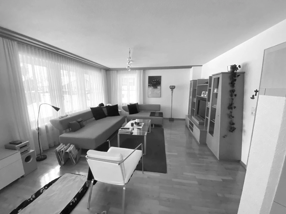 Wohnzimmer im Einfamilienhaus Bohle vor der Generalsanierung: Blick auf Polstermöbel, Couchtische, Teppich, weiße Stühle und Holzparkett.