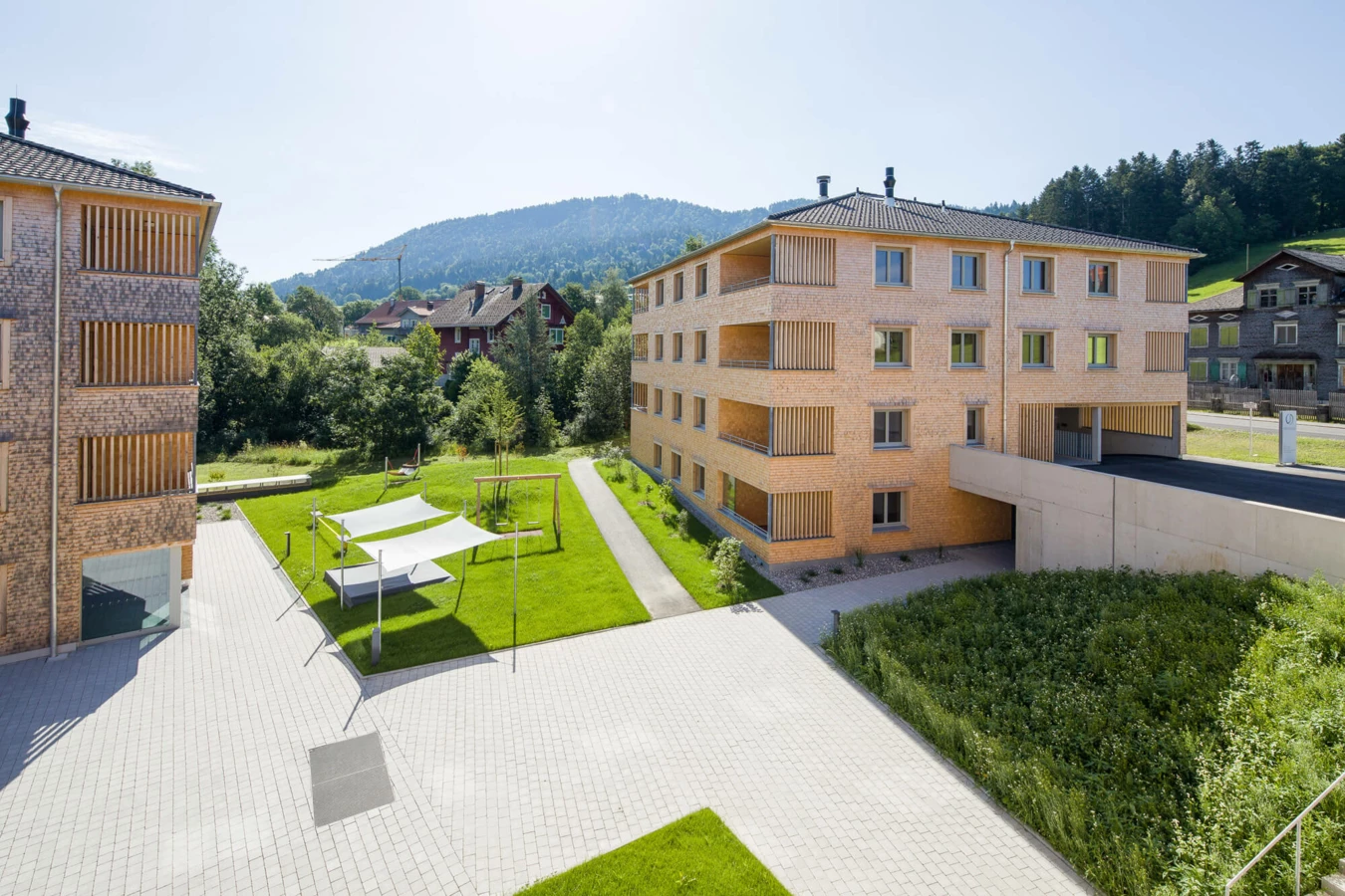 Moderne Wohnanlage Schwarz in Alberschwende mit Holzbalkonen und großzügiger Grünfläche am sonnigen Tag.