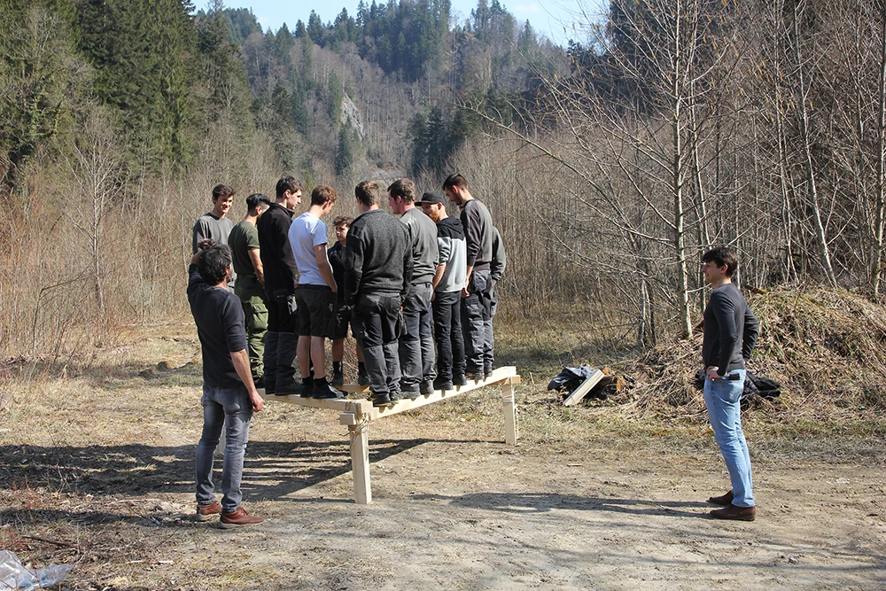 Eine Gruppe junger Männer balanciert auf einer Holzkonstruktion während des Lehrlingstages 2017 in der Natur.