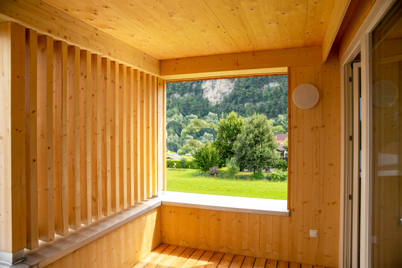 Holzverkleideter Balkon oder Loggia mit Blick auf grüne Wiesen, Bäume und einen bewaldeten Berg im Hintergrund (Hellbrunnenstraße).