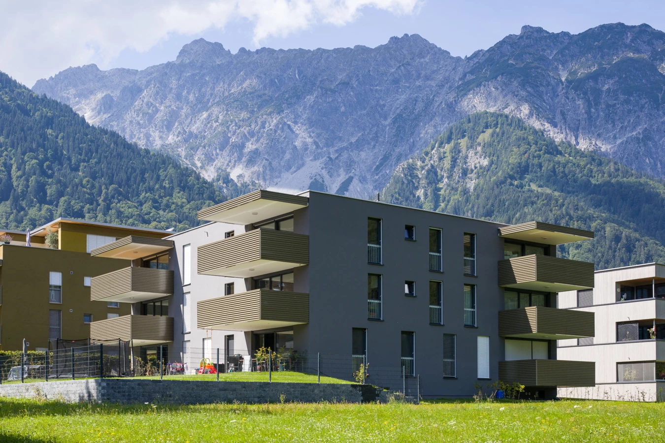 Moderne Wohnanlage mit dunkler und ockerfarbener Fassade und mehreren Balkonen im alpinen Stil in Vandans, umgeben von grünen Bergen und Wiesen (Bahnhofstraße, Bahnhofsstrasse).