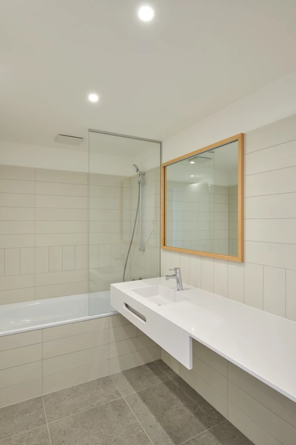Modernes Badezimmer mit weißer Badewanne, Glasduschabtrennung und einem langen, schwebenden Waschtisch mit Spiegel (Apollogasse).