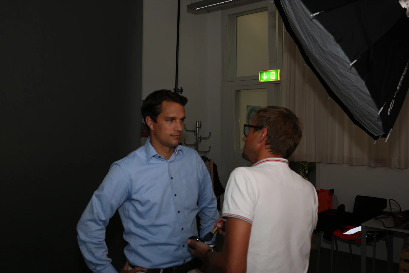 Zwei Männer unterhalten sich bei einem Fotoshooting, ein Softbox-Blitzschirm ist sichtbar.