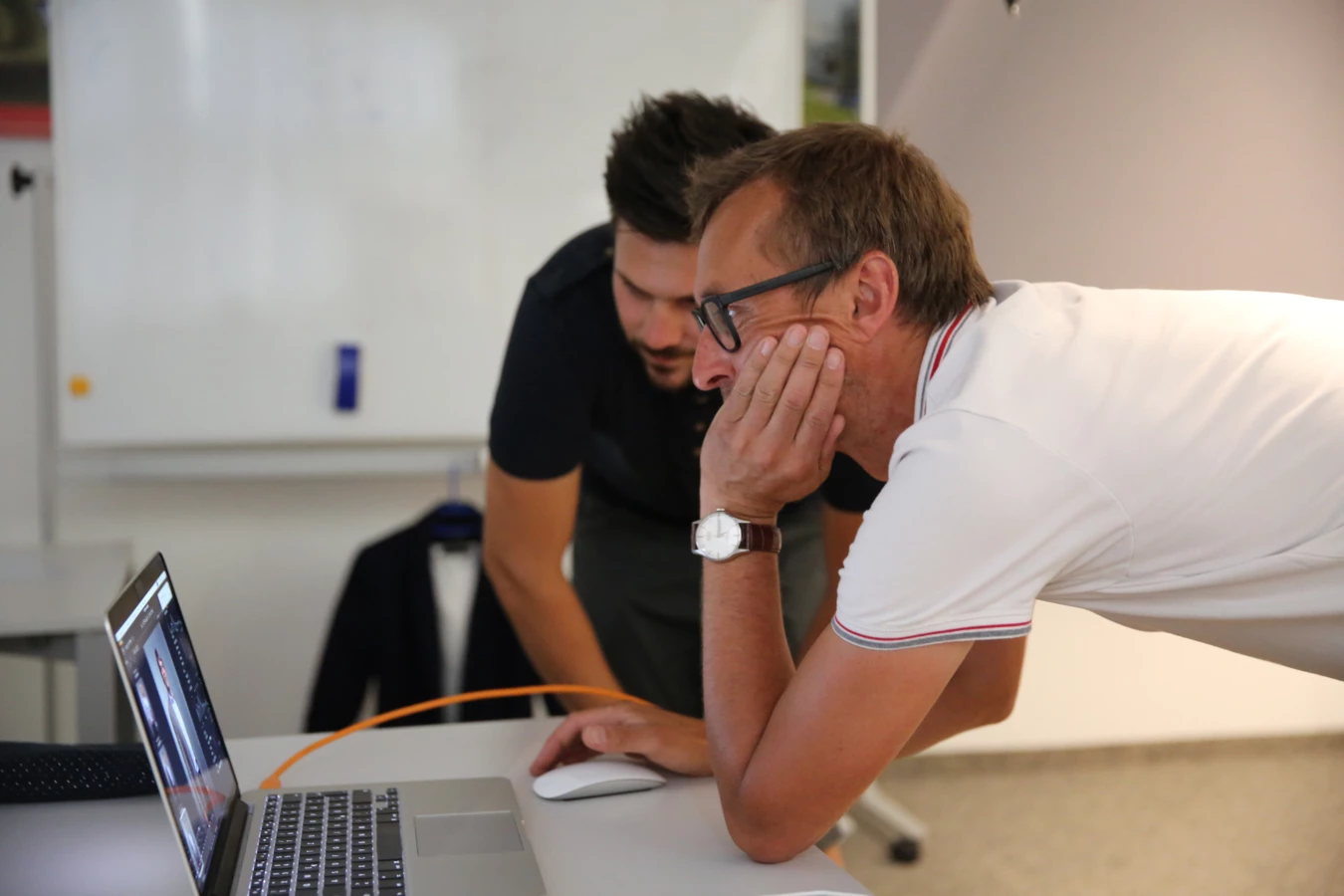 Zwei Männer betrachten konzentriert den Bildschirm eines Laptops auf einem Schreibtisch, einer mit der Hand am Kinn.