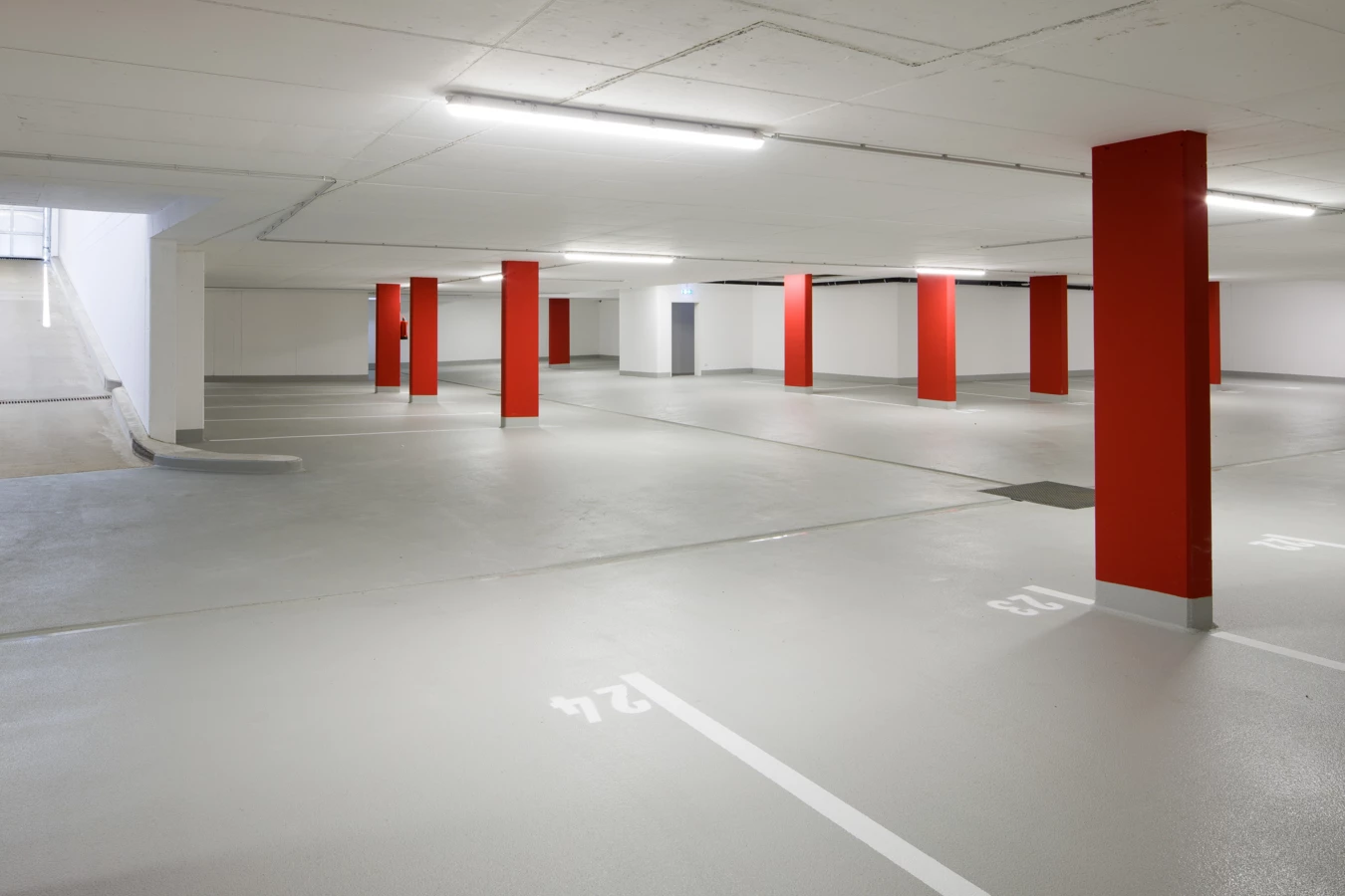 Leere Tiefgarage an der Unterhochstegstraße mit roten Säulen, weißen Parkplatzmarkierungen, hellgrauem Boden und Rampenzufahrt.