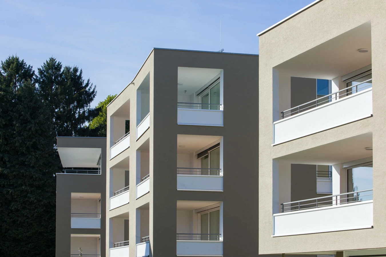 Moderne Wohngebäude mit beigen Fassaden und weißen Balkonen in der Wohnanlage Widum Lustenau.