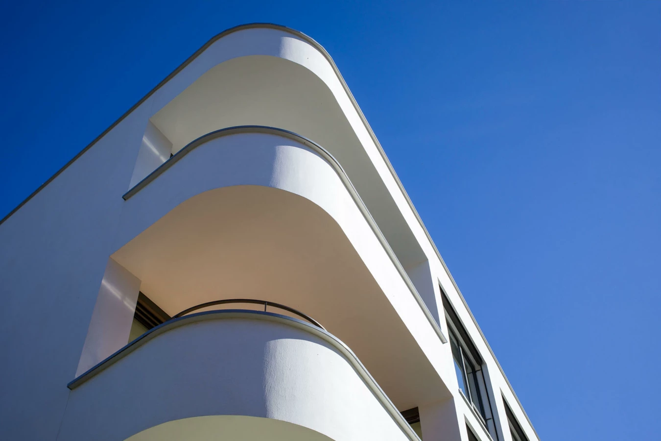 Eine Nahaufnahme der abgerundeten, hellweißen Balkone eines modernen Gebäudes vor einem klaren blauen Himmel bei Tageslicht (Wolf-Huber-Straße, Wohnanlage, Feldkirch).
