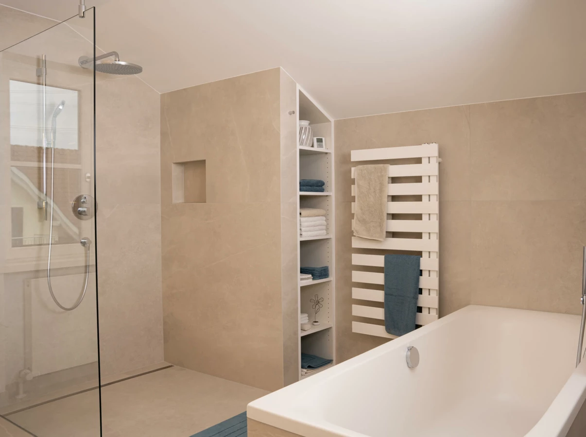 Modernes Bad mit beigen Fliesen, bodengleicher Dusche, Badewanne, Handtuchheizung und Einbauregal mit Handtüchern (Generalsanierung, Bohle).