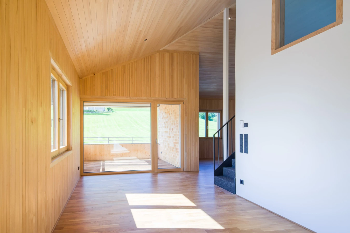 Moderner Wohnraum mit Holzverkleidung an Wänden und Decken, großen Fenstern, Balkon und Treppe, in der Wohnanlage Schwarzen, Alberschwende.
