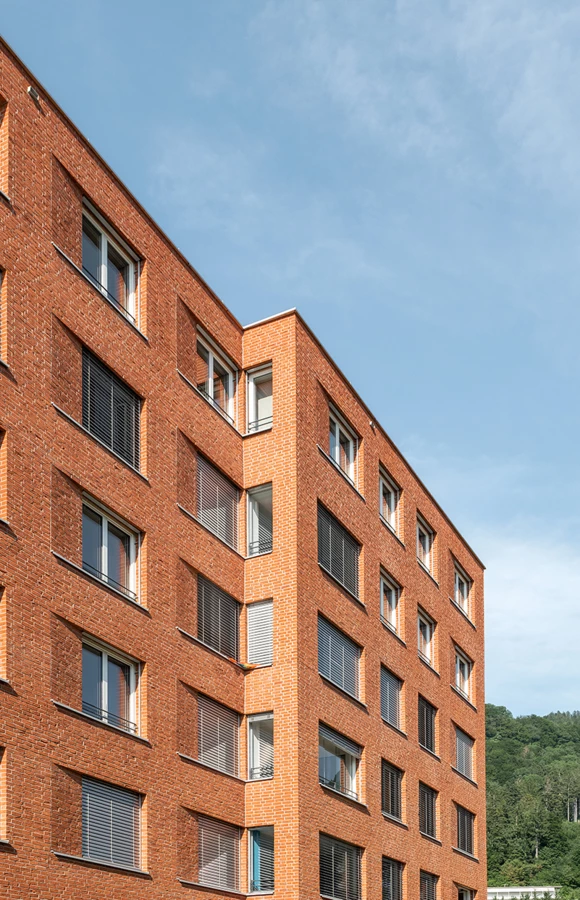 Wohngebäude mit orangebrauner Ziegelfassade und Fenstern mit Jalousien, im Sonnenlicht unter blauem Himmel (Seeblick, Lochau)