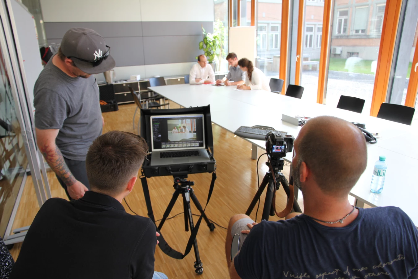 Eine Gruppe von vier Personen filmt eine Besprechung in einem modernen Büro und verwendet dafür professionelle Fotoausrüstung.