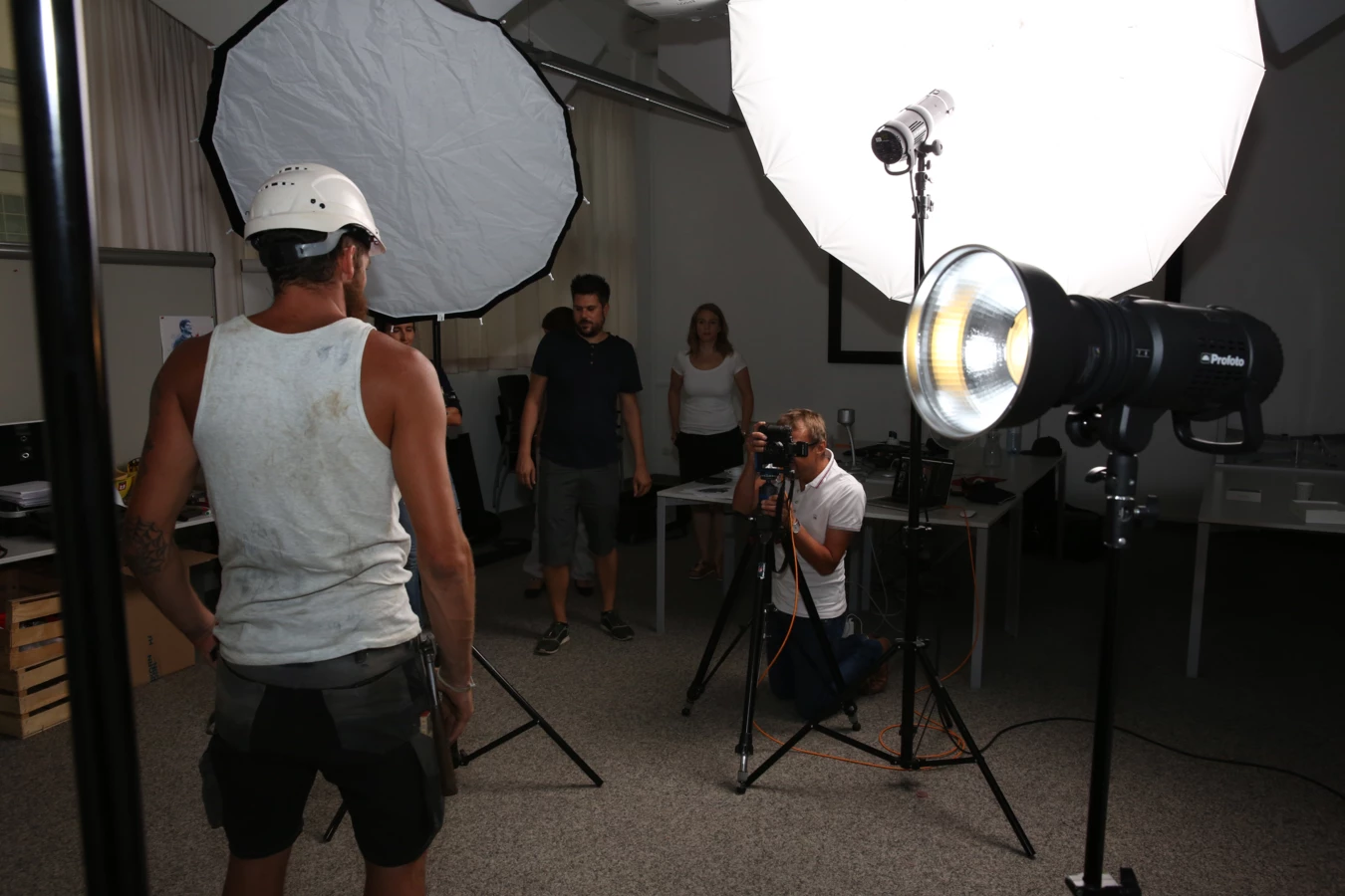 Ein Fotoshooting im Innenbereich mit einem Mann in Bauarbeiterkleidung als Model und Personen an Kameras und Beleuchtung