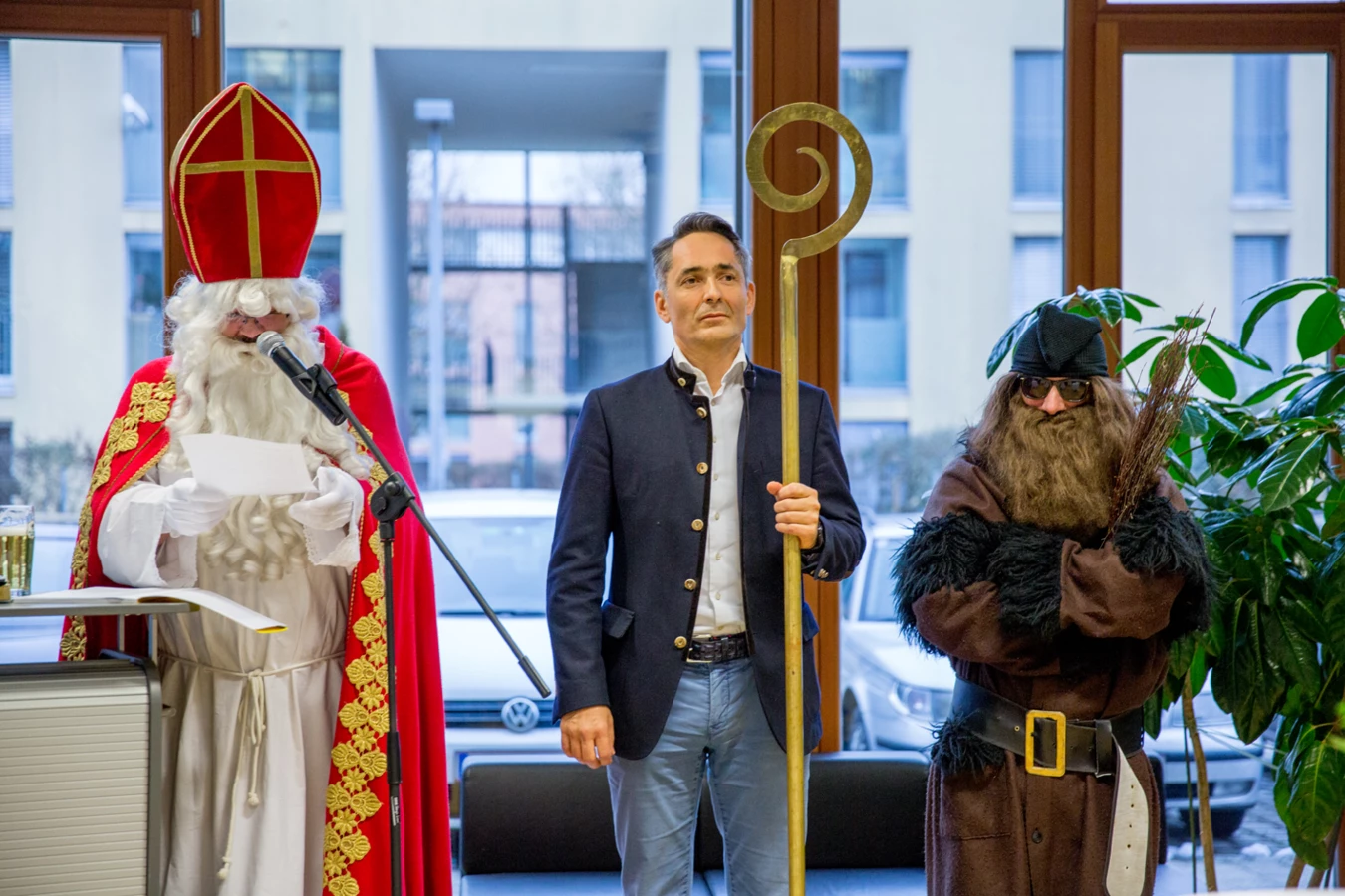 Ein Mann im Nikolauskostüm spricht ins Mikrofon, neben ihm stehen ein Mann im Blazer und ein Knecht Ruprecht (Hubert, Geburtstag).