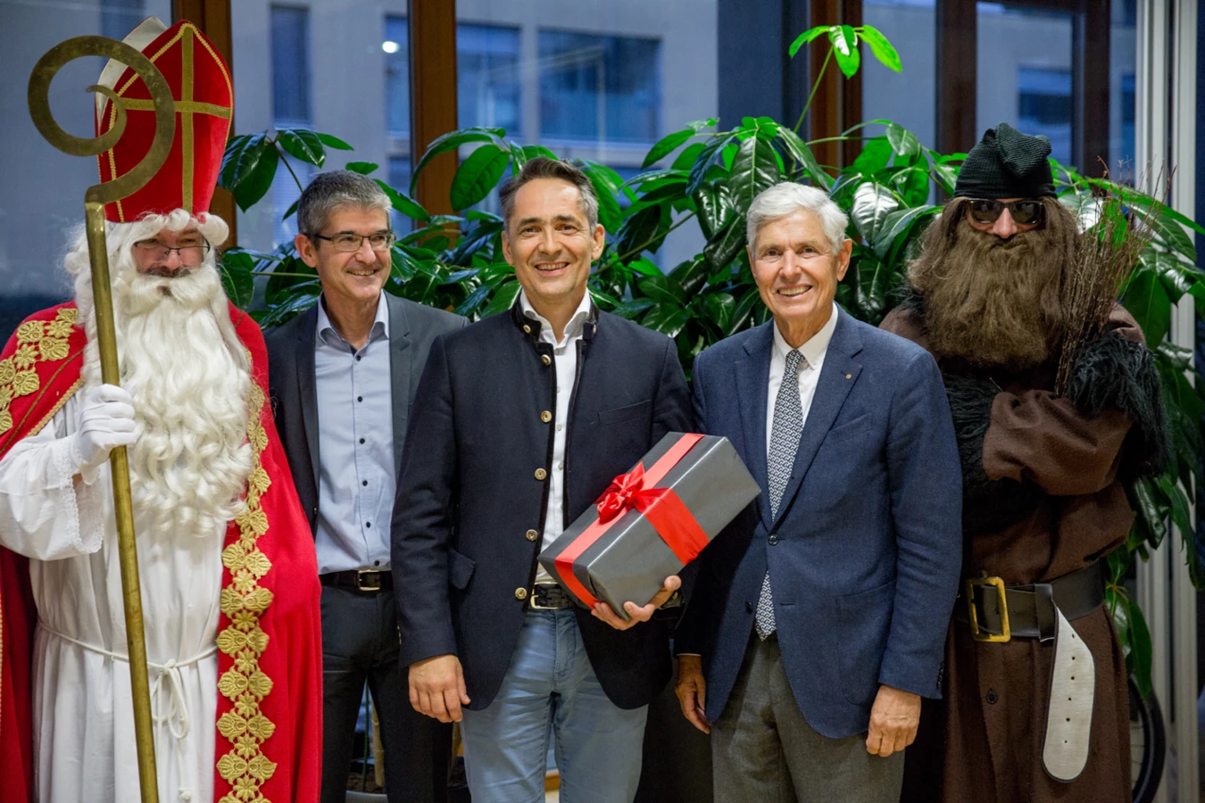 Fünf Männer posieren für ein Foto, zwei von ihnen sind als Nikolaus und Krampus verkleidet, inmitten von Pflanzen (Hubert, Geburtstag).