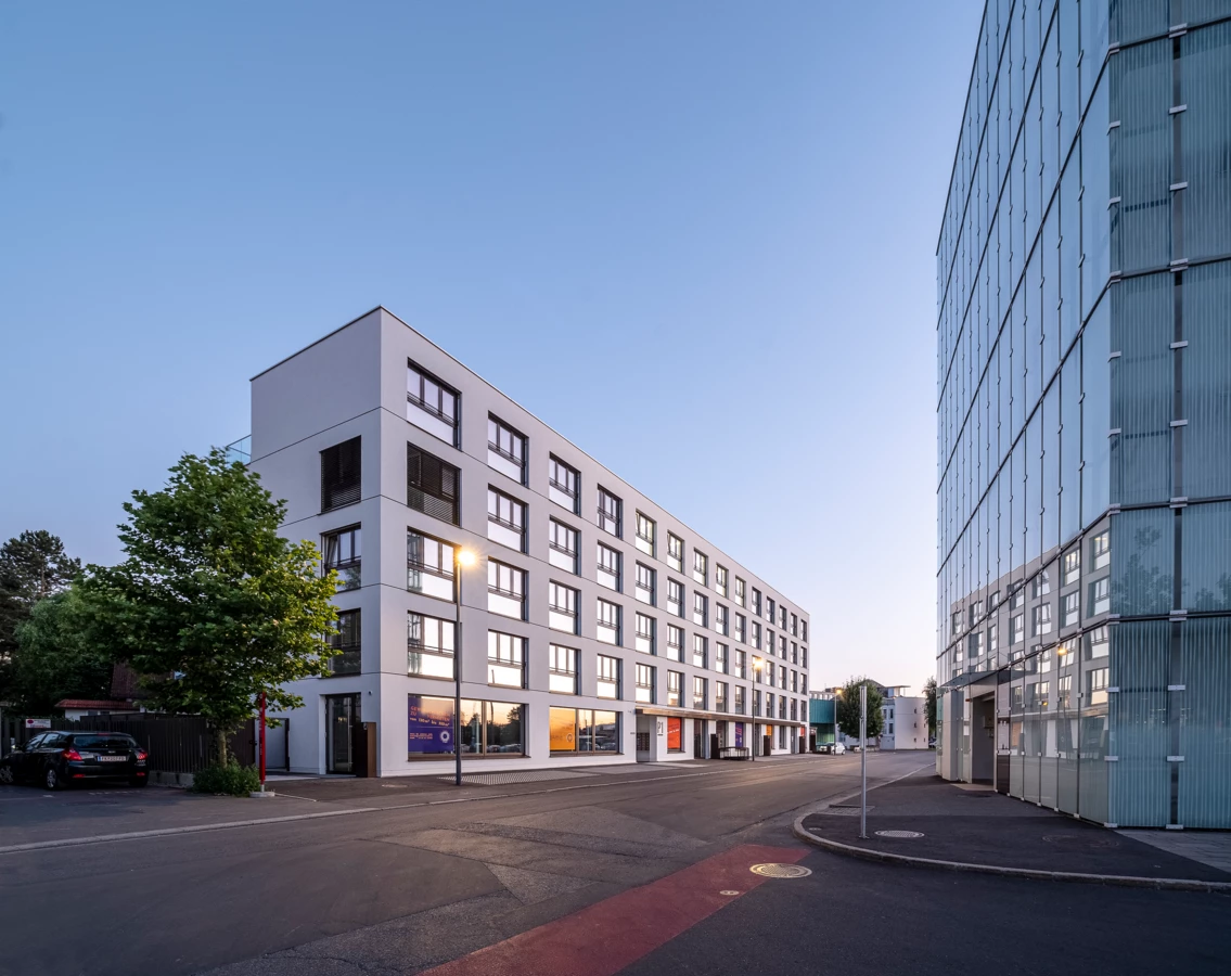 Modernes, weißes Verwaltungsgebäude mit reflektierenden Fenstern und daneben ein verglastes Bürogebäude in Dornbirn.