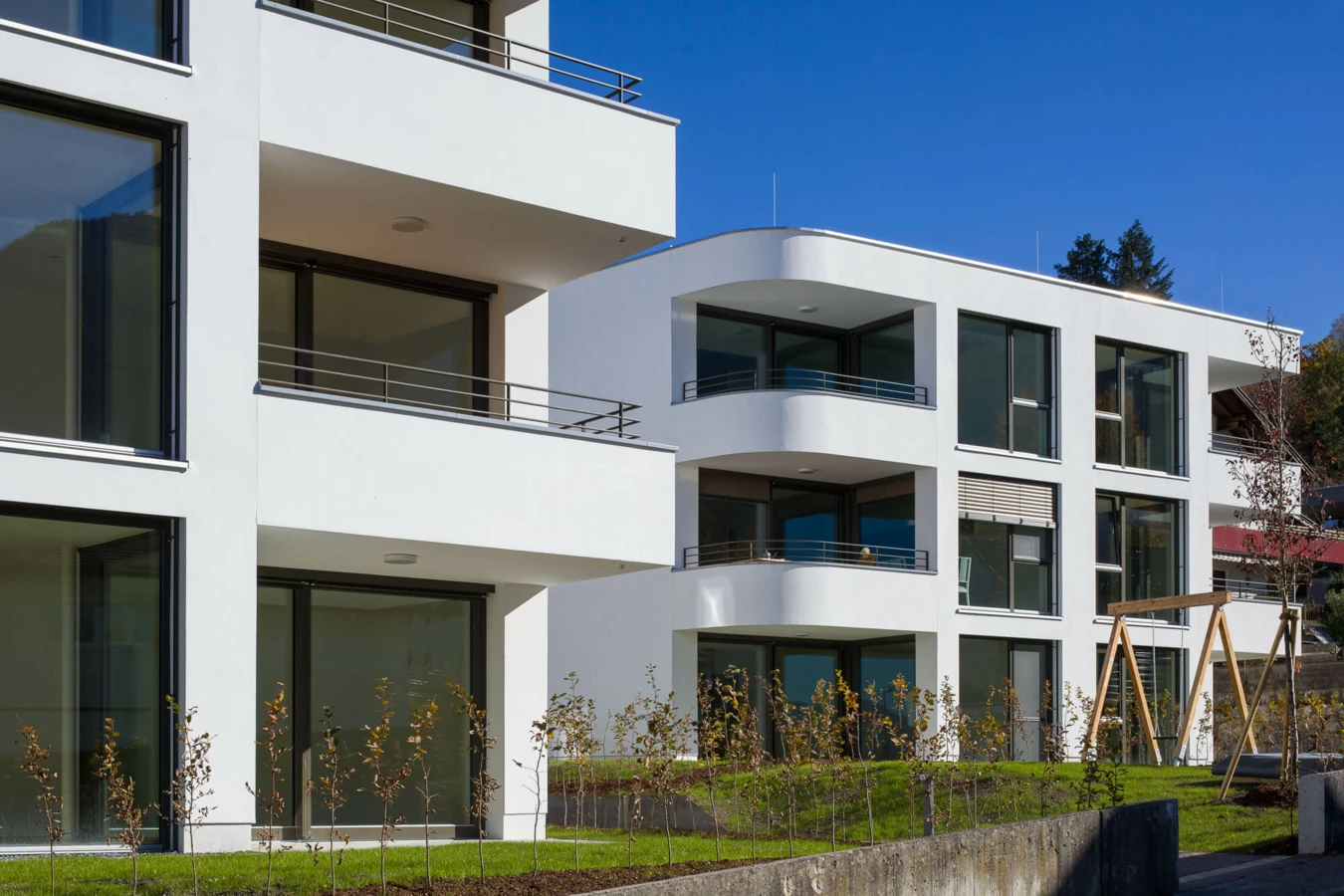 Moderne Wohngebäude mit weißen Fassaden, großen Fenstern und Balkonen unter blauem Himmel in Feldkirch (Wolf-Huber-Straße, Wohnanlage).