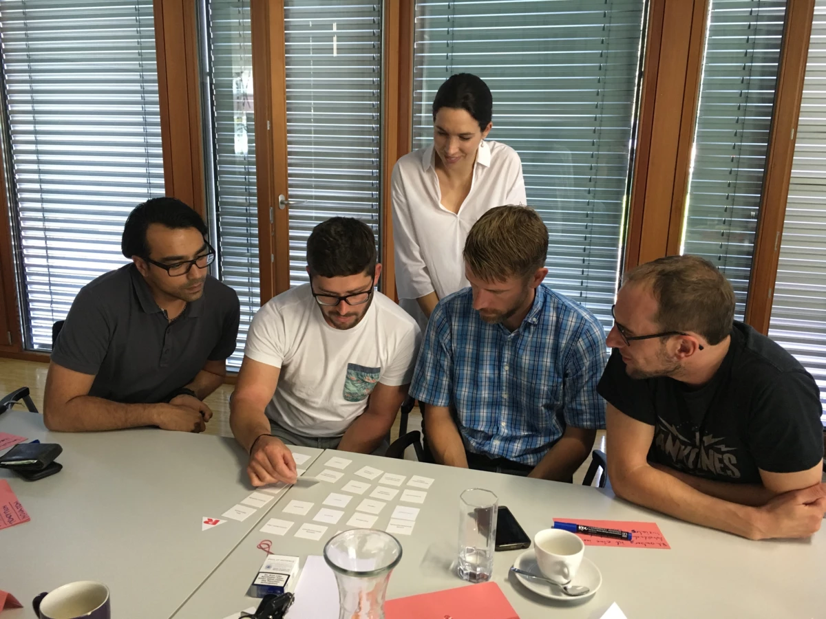 Fünf Personen, darunter eine Frau und vier Männer, arbeiten konzentriert an einem Tisch mit vielen weißen Karten und roten Notizen (Workshop).