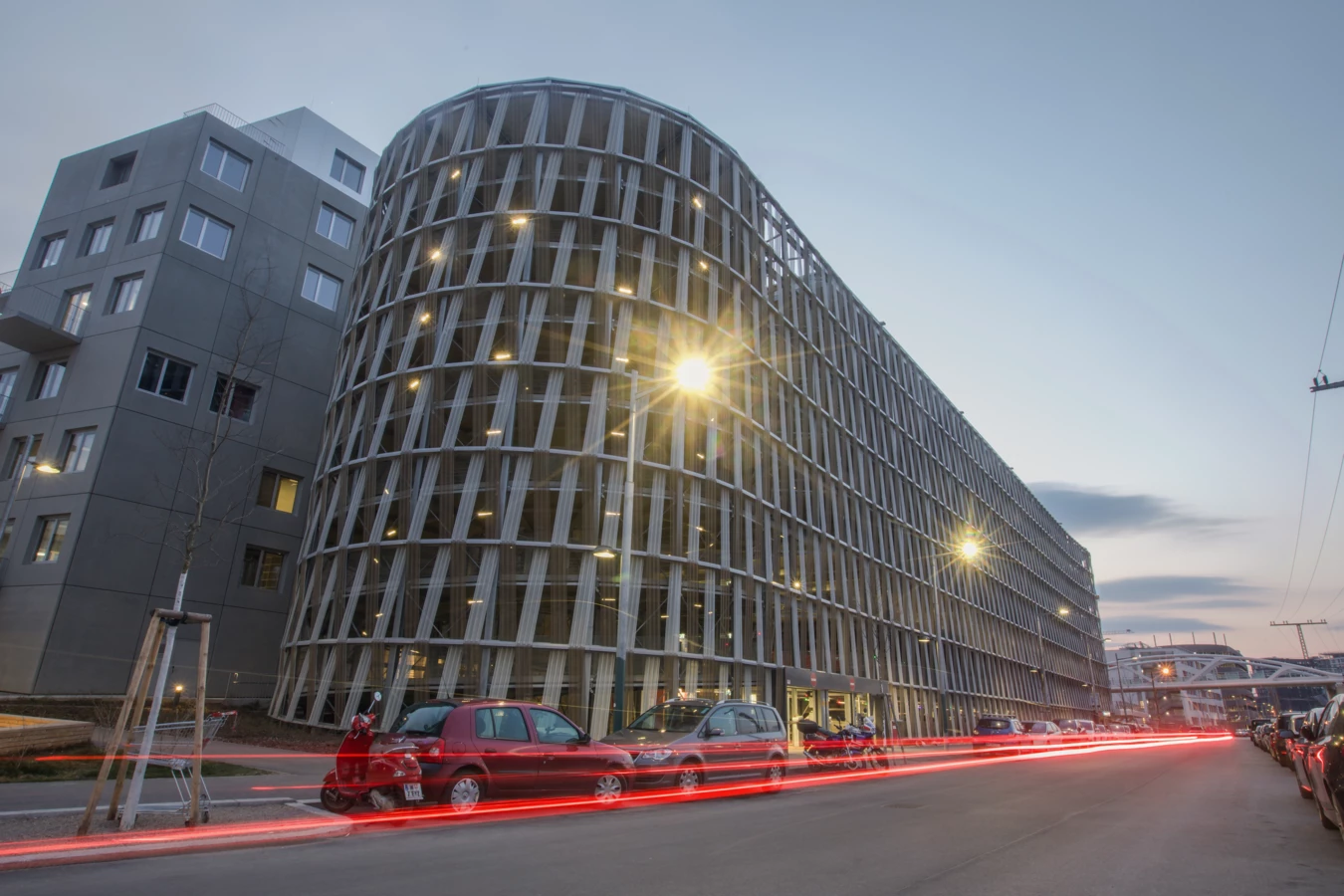Hochgarage am Wiener Hauptbahnhof bei Abenddämmerung mit dynamischen roten Lichtspuren von vorbeifahrenden Autos (Wien).