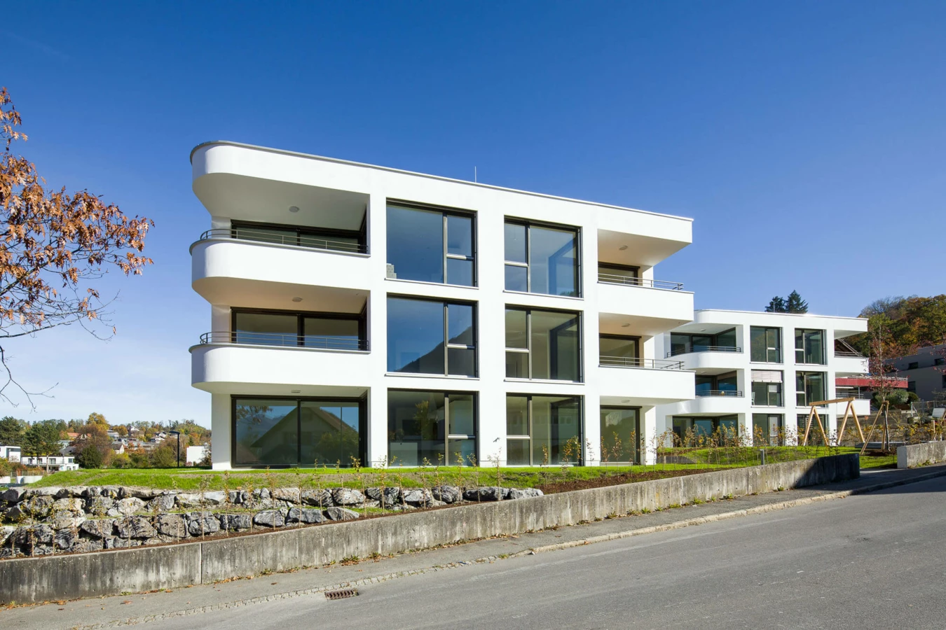 Moderne weiße Wohnanlage mit großen Fenstern und Balkonen unter blauem Himmel in Feldkirch (Wolf-Huber-Straße).