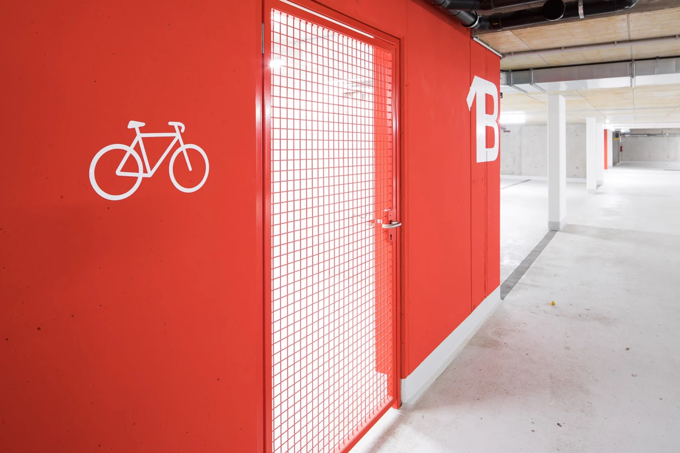 Roter Wandbereich in einer Tiefgarage mit Fahrradsymbol und "B" Markierung, daneben eine rote Gittertür zur Fahrradgarage (Baeumlequartier).