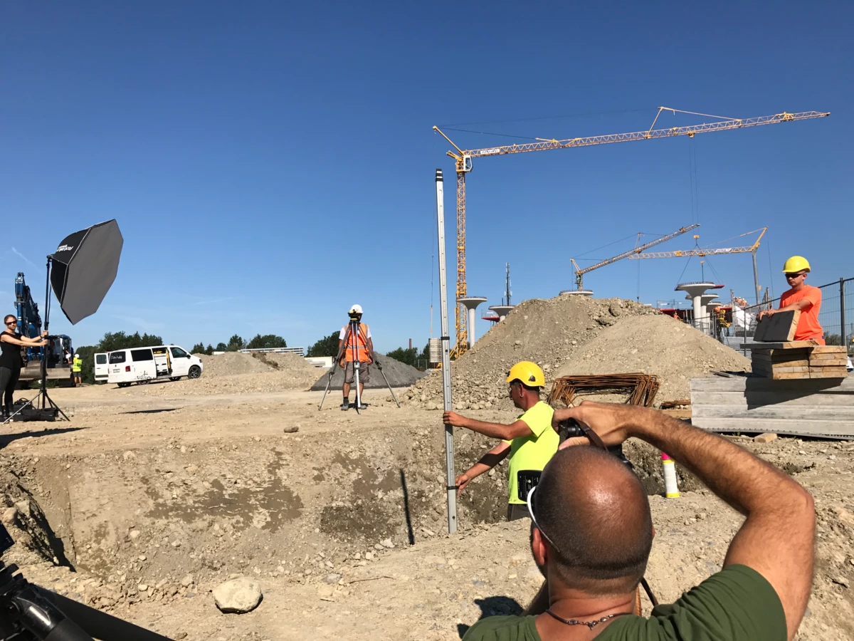 Team bei einem Fotoshooting auf einer Baustelle mit Kranen und Erdhügeln unter blauem Himmel