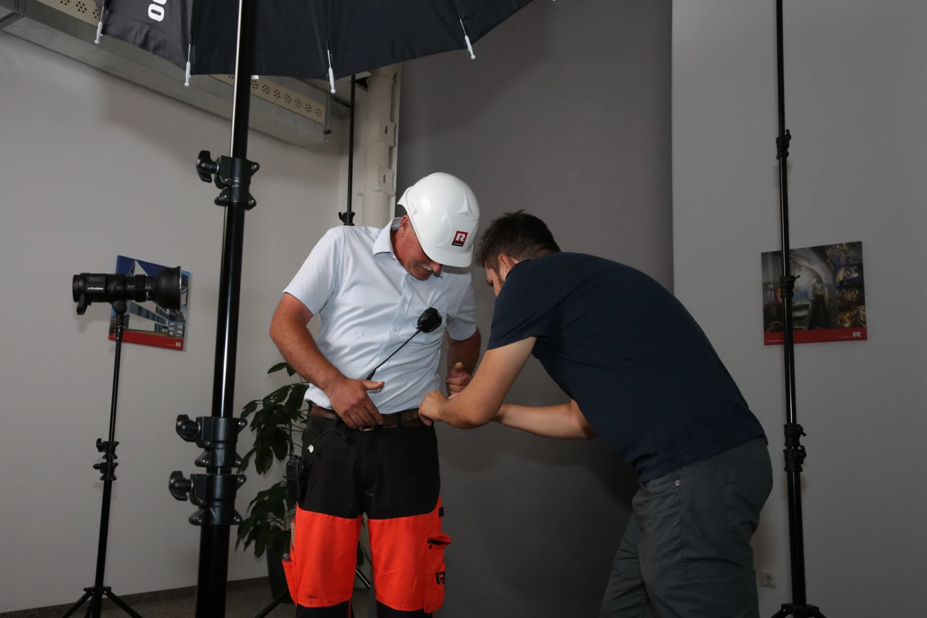 Zwei Männer bei einem Fotoshooting. Einer der Männer trägt Arbeitskleidung von Rhomberg Bau und einen Schutzhelm.