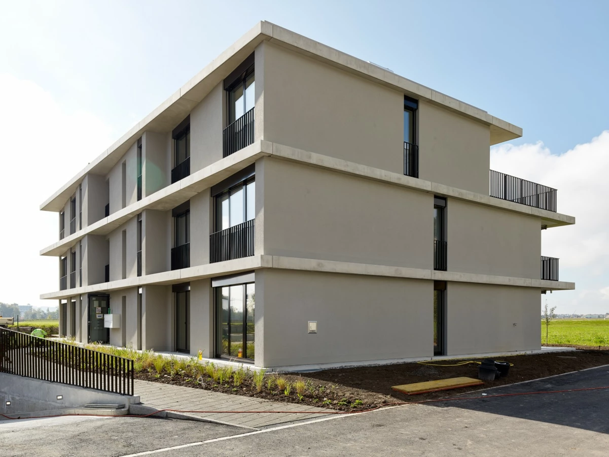 Moderne, mehrstöckige Wohngebäude in Egerkingen mit grauer Fassade, Balkonen und umliegender Grünfläche an einem sonnigen Tag.