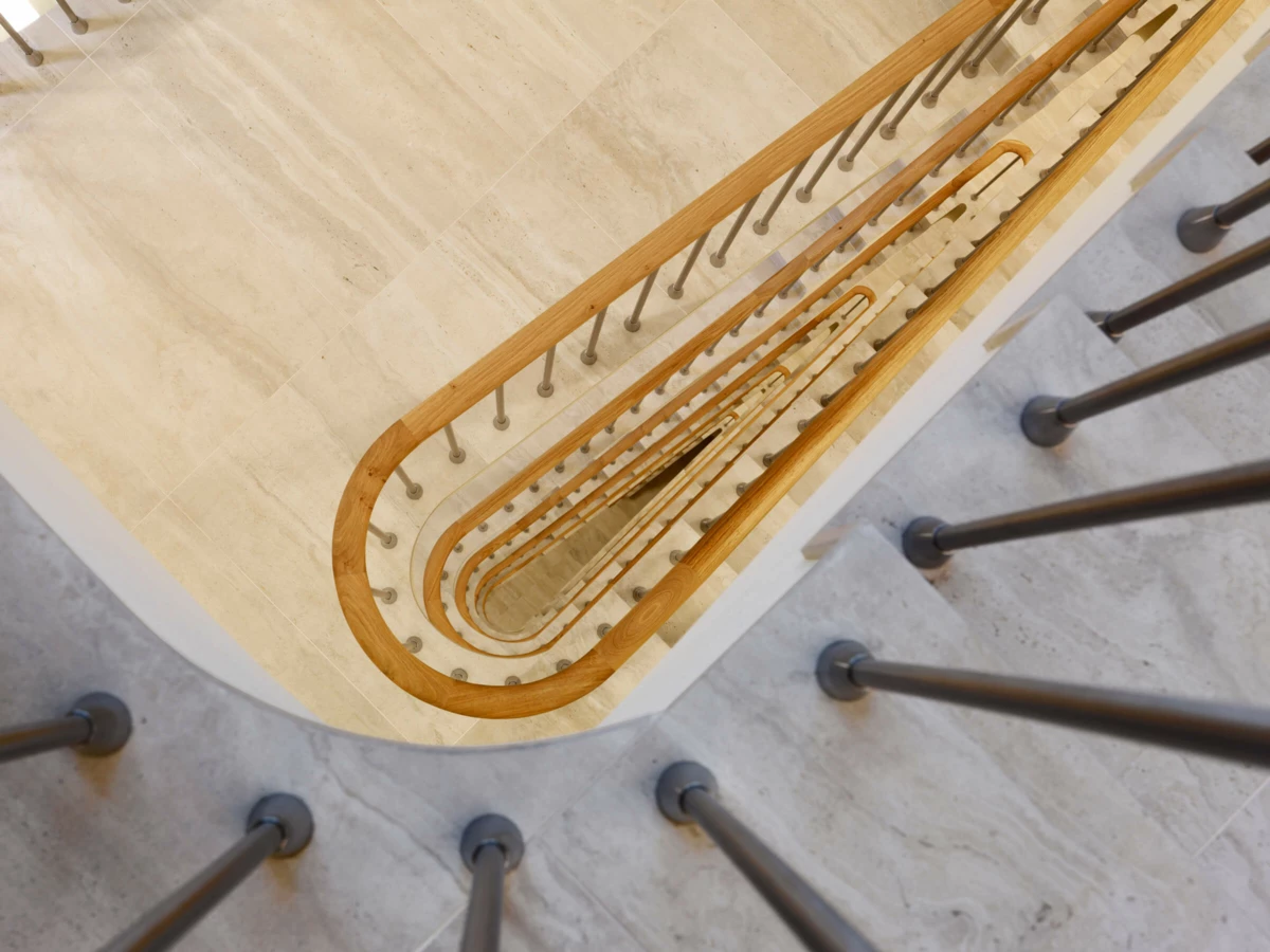 Blick von oben auf eine spiralförmige Treppe aus hellem Marmor mit Holzhandlauf und Metallgeländer im Gebäude Multergasse in St. Gallen.